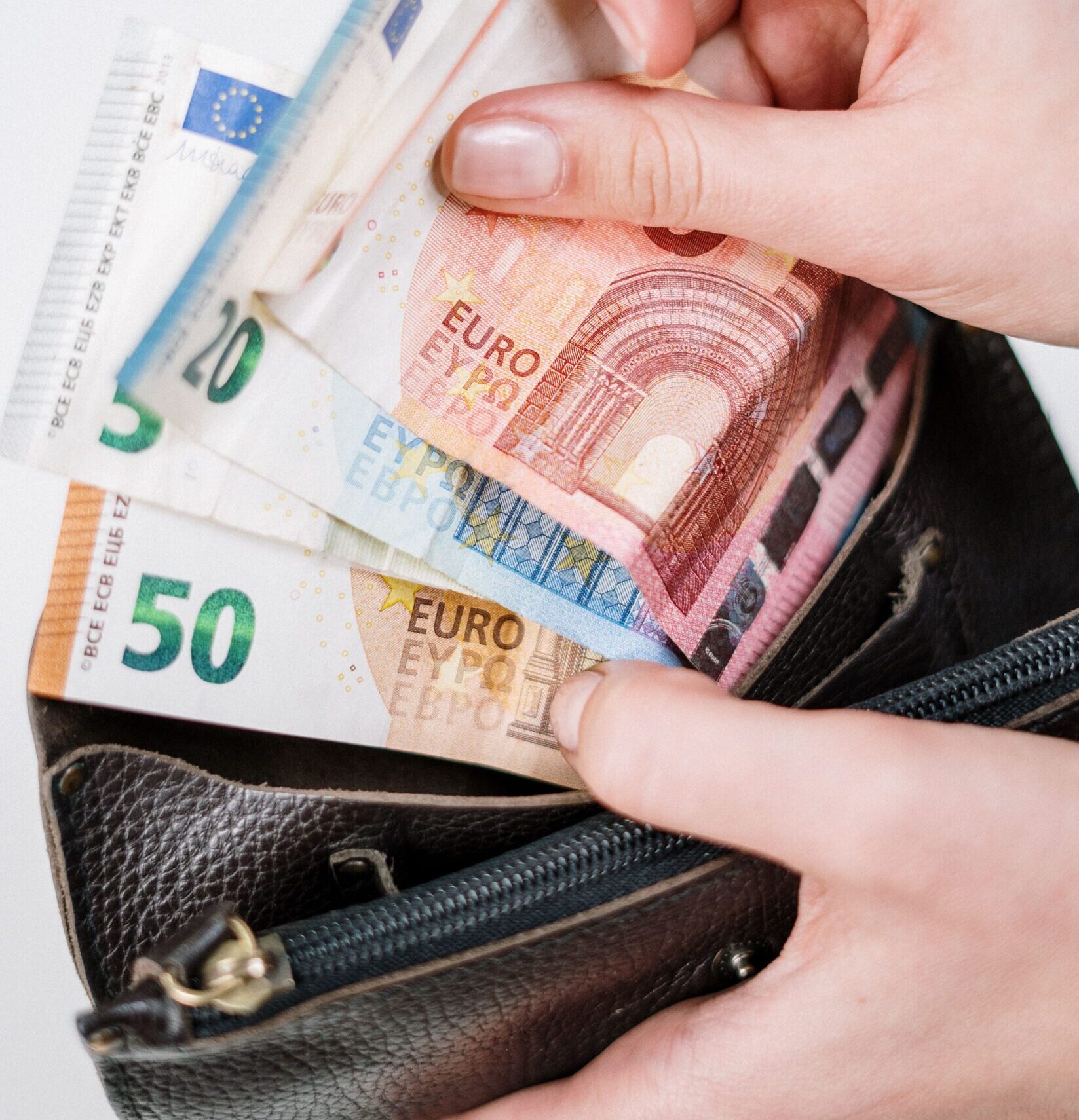 Close-up of hands counting euro banknotes from a leather wallet, representing financial transactions.